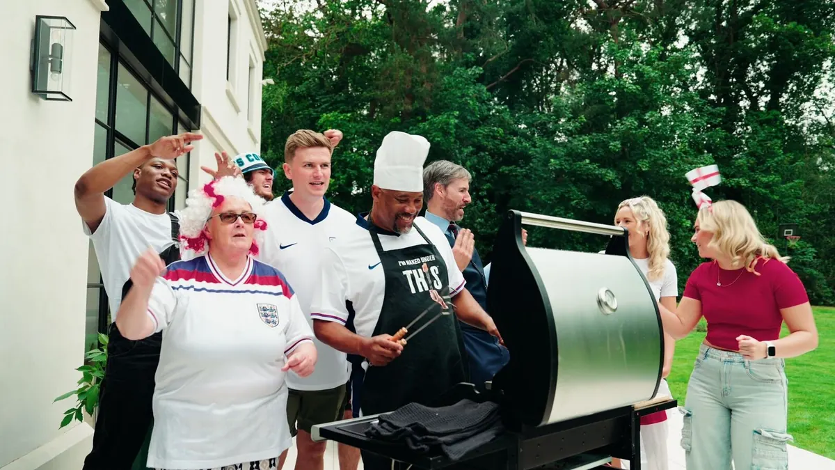 John Barnes at a barbecue in a THIS apron, surrounded by fans in England shirts at a big house.