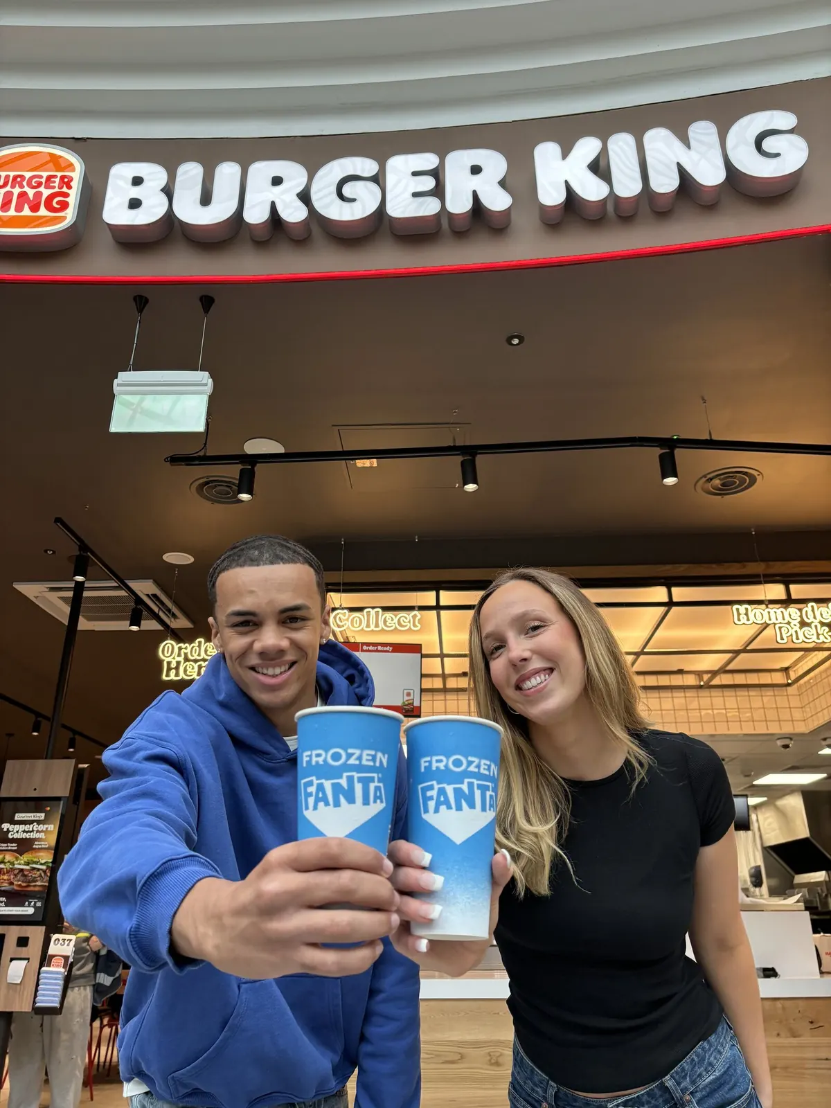 Two people raising Fanta Frozen cups inside a Burger King.