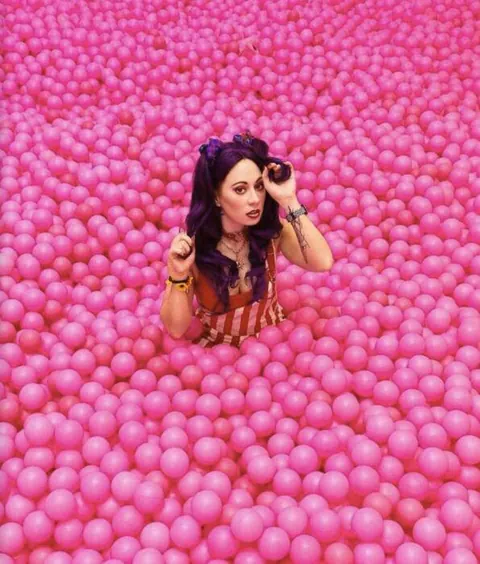 A woman lying in a ball pit full of pink balls at Selfie Factory.