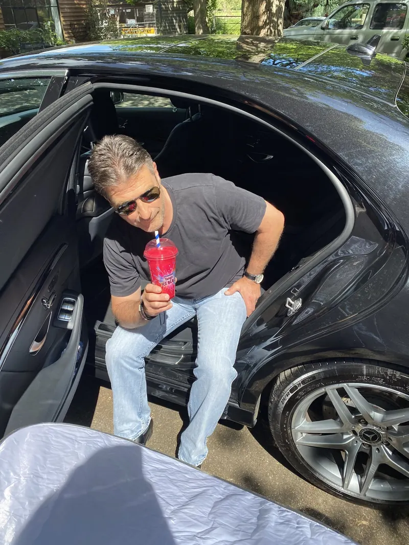 A lookalike holding a Tango Ice Blast in the open door of a black car.