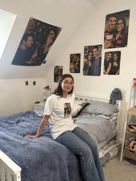 The character on her bed, under a wall of photos of herself and her date.